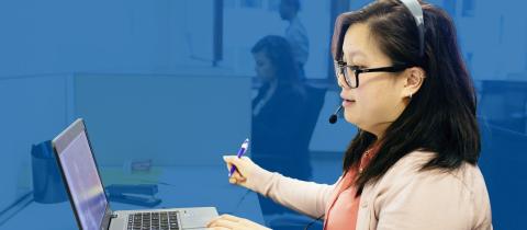 A young woman with black hair speaking with a customer on her headset at her computer