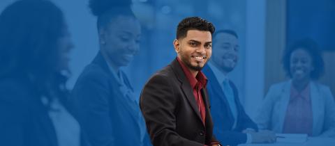 A smiling man in a suit surrounded by coworkers looking toward the camera