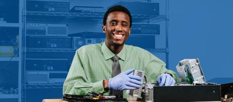 A smiling man in a dress shirt and tie sitting at a desk and smiling at the camera