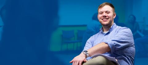 A smiling man sitting down with his legs crossed, looking toward the camera